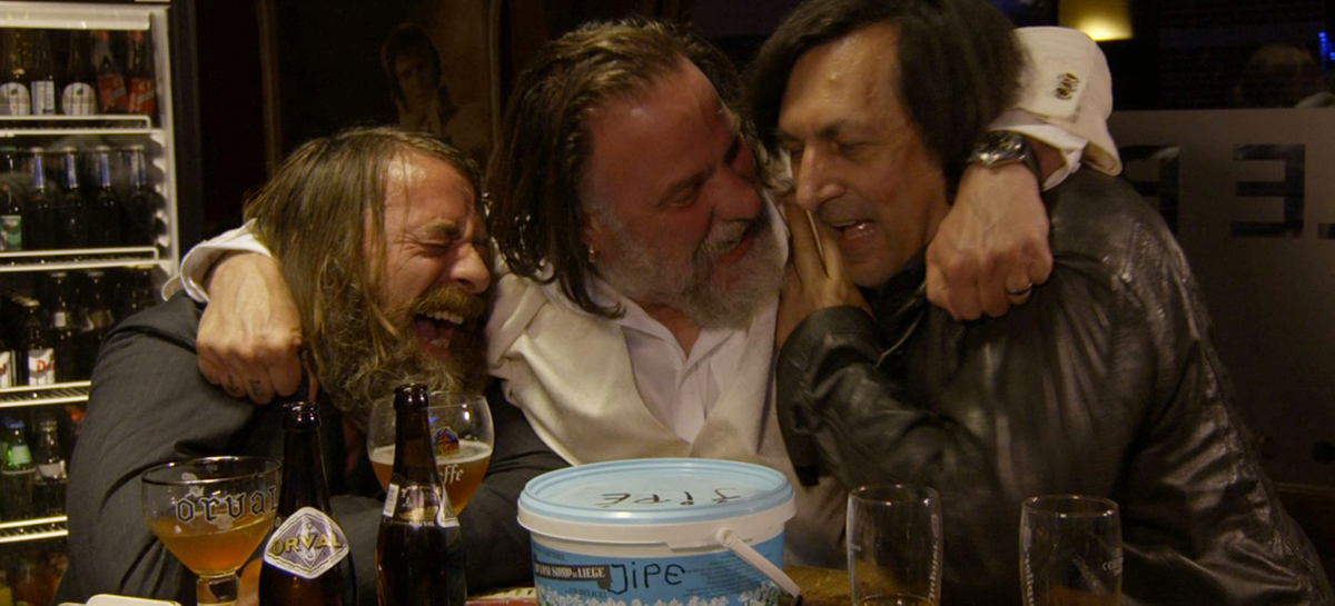 Trois acteurs rient dans un bar, avec des bières sur une table