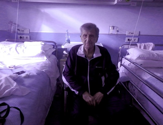 Un vieil homme assis entre deux lits d'hôpital