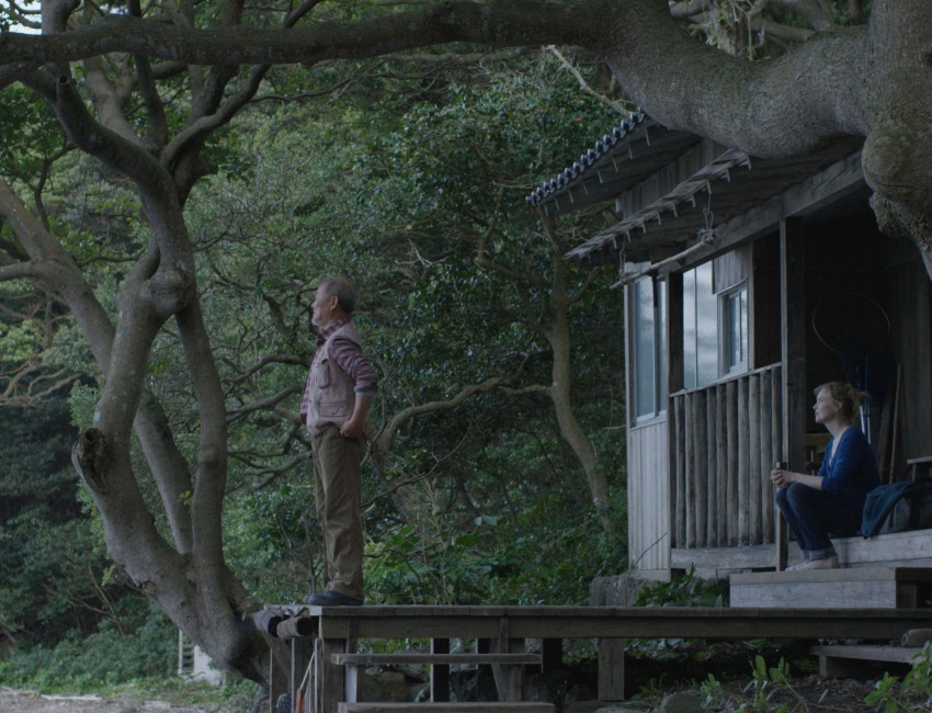 Dans le bois, près d'une cabane, un homme regarde au loin. Une femme (Isabelle Carré) est sur le pas de la porte de la cabane.