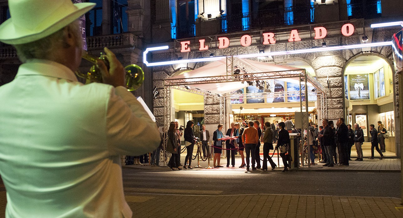 Un homme en costume blanc joue de la trompette en face du cinéma Eldorado.