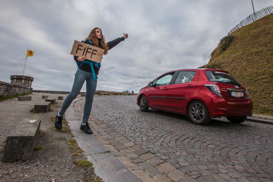 Une jeune fille avec un carton FIFF dans les mains, elle fait du stop.