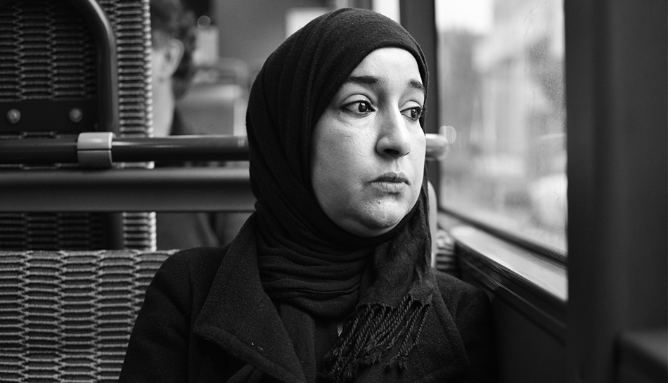 Une femme avec un voile regarde dehors, l'air pensif.