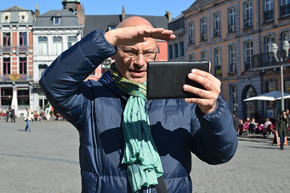 Un monsieur regarde difficilement sa tablette dû au soleil sur la Grand place de Mons.