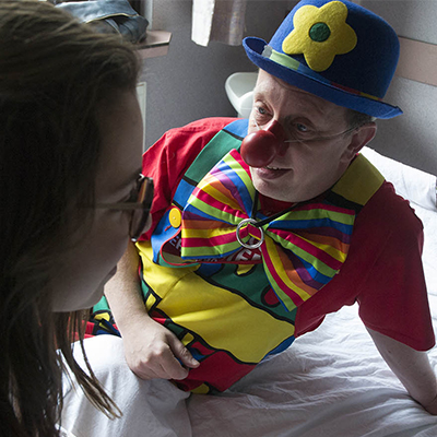 Un clown est allongé sur un lit et écoute une jeune fille malade.