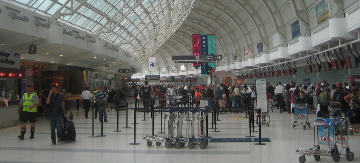 hall d'aéroport rempli de gens. Des charrettes sont à l'avant-plan.