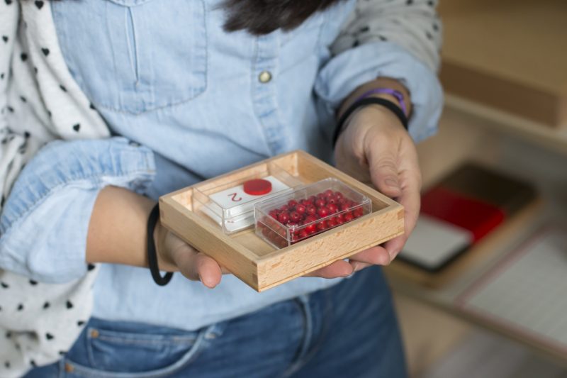 Institutrice tenant en main un outil d'apprentissage des mathématiques via des perles rouges