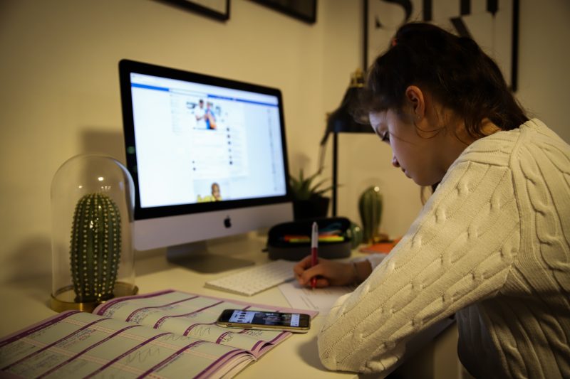 jeune fille faisant ses devoirs avec l'aide de son smartphone et de son ordinateur