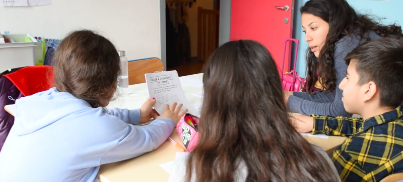 Adulte donnant court à des enfants de dos, dans une classe colorée