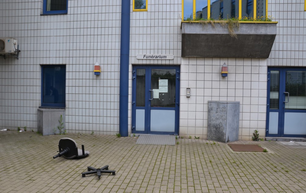 Ecriteau « funérarium » au-dessus de la porte d’entrée d’un bâtiment devant lequel gît une chaise de bureau cassée.