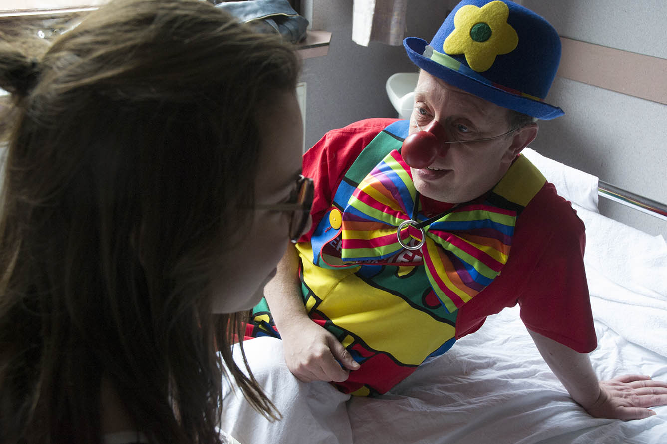Un clown est allongé sur un lit et écoute une jeune fille malade.
