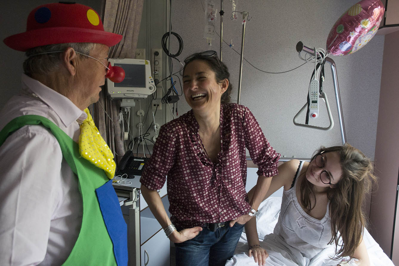 Une jeune fille malade et sa mère rient en regardant le clown dans une chambre d'hôpital.
