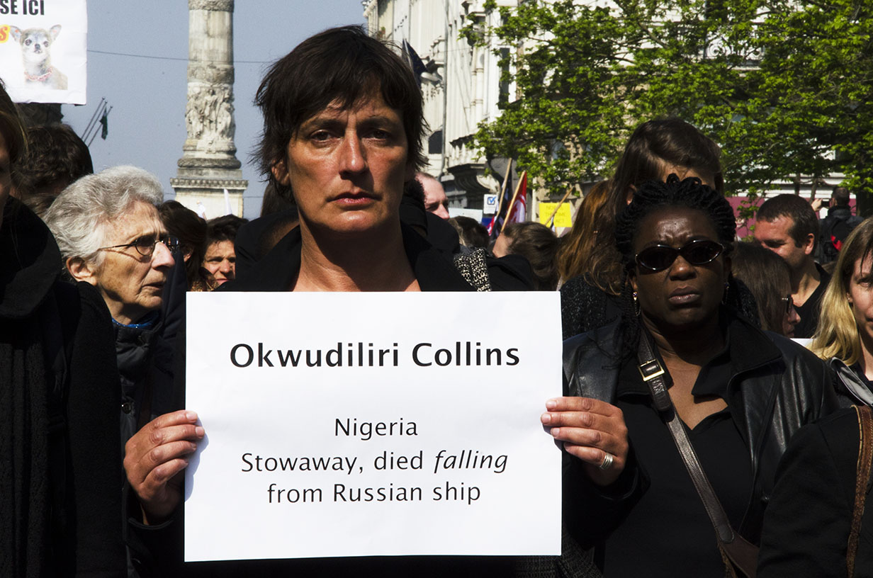 Une femme tient une pancarte sur laquelle est inscrit 'Okwudiliri Collins, Nigeria, Stowaway, died falling from Russian ship'.