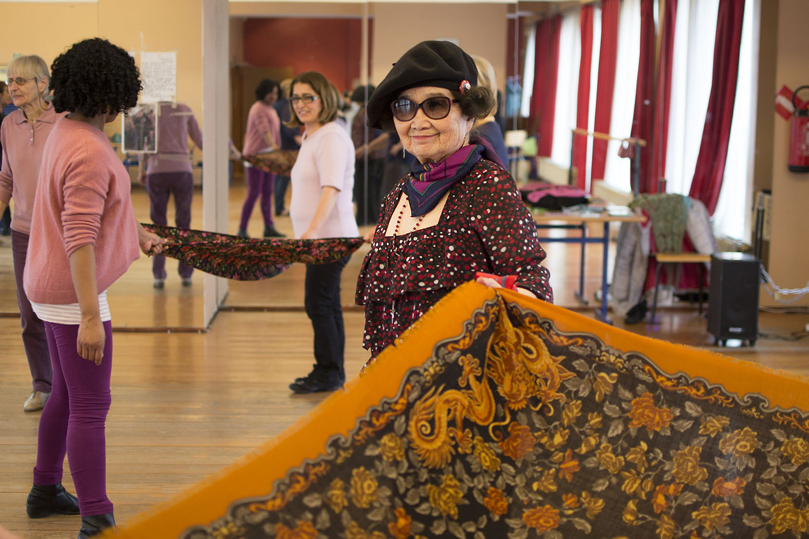 Une dame âgée, aux traits asiatiques, tient dans sa main gauche un foulard orange.